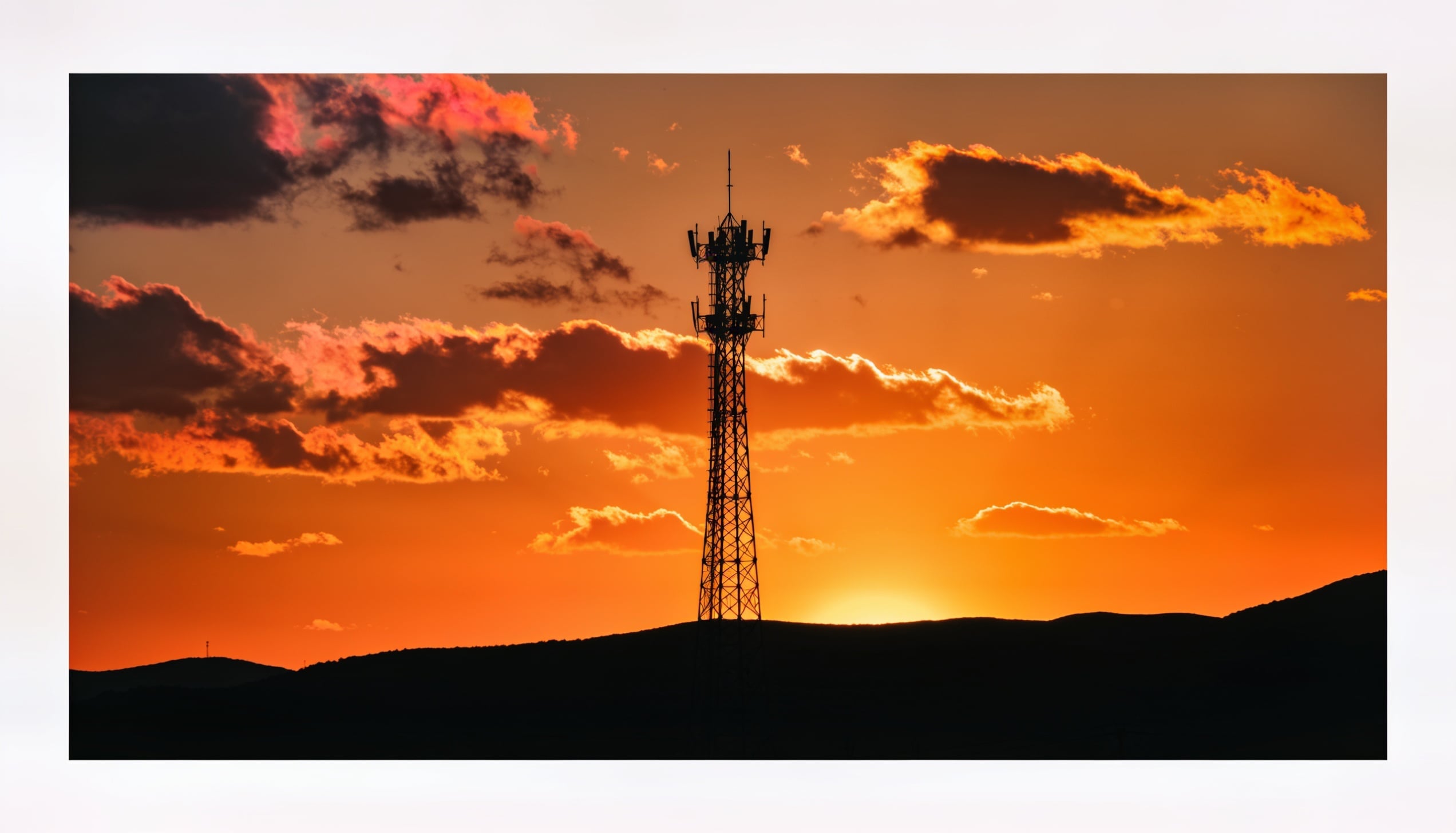 A towering cell tower silhouetted against a vibrant orange sunset sky.